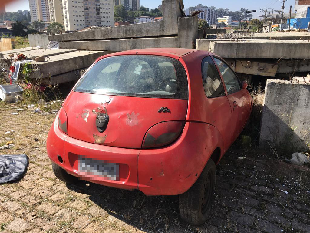 Traseira de um carro vermelho abandonado em um pátio